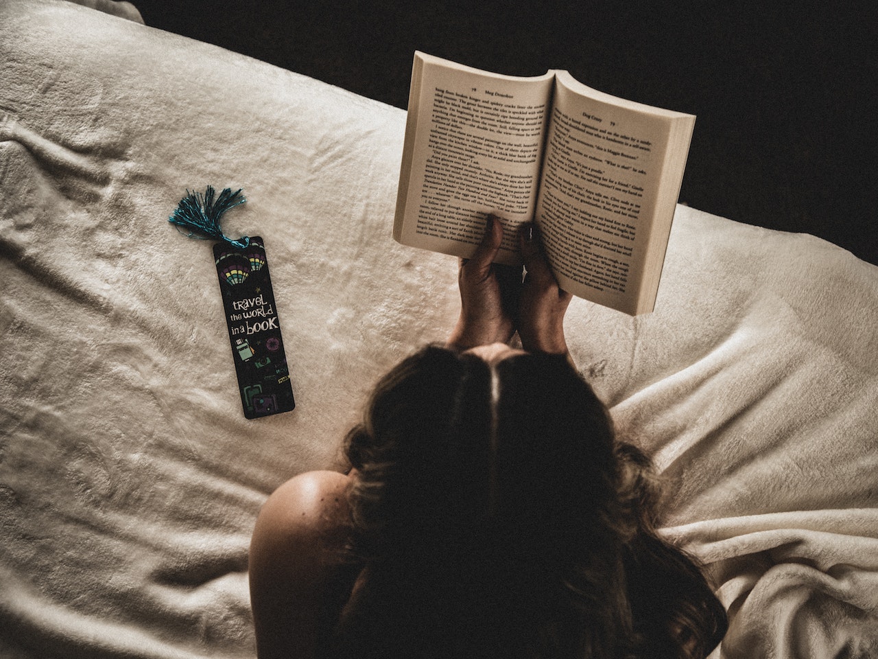 Na zdjęciu widzimy kobietę, która siedzi na łóżku i z pochylonym nad książką czołem skupia się na lekturze. Książka, którą trzyma w dłoniach, jest z gatunku literatury obyczajowej. Widać, że kobieta jest w pełni pochłonięta historią i emocjami, jakie niesie ze sobą lektura. Widoczne na zdjęciu detale, takie jak wygodne poduszki i koce, sugerują, że czytanie jest dla niej sposobem na relaks i odpoczynek po ciężkim dniu. Takie podejście do literatury obyczajowej, która często porusza trudne tematy z życia codziennego, pokazuje, że ta forma sztuki może być zarówno inspirująca, jak i relaksująca. To zdjęcie jest doskonałym wizualnym odzwierciedleniem siły i pozytywnego wpływu, jaki może mieć literatura obyczajowa na nasze życie. Zachęca do sięgnięcia po książkę z tego gatunku i doświadczenia na własnej skórze, jakie wartości i emocje potrafi przynieść literatura obyczajowa